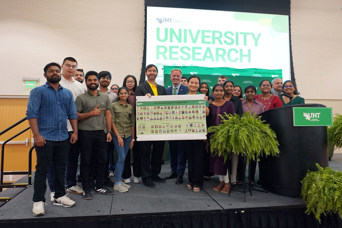 Students posing in group photo on stage with UNT President Keller.
